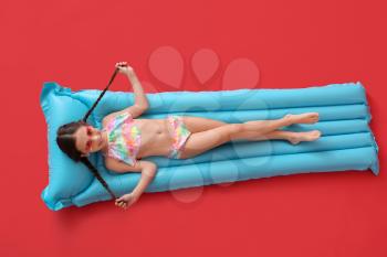 Cute little girl lying on inflatable mattress against color background�