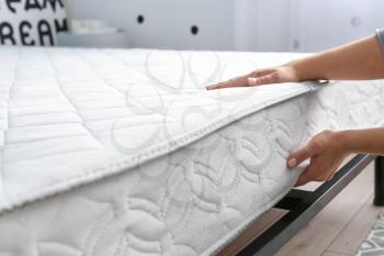 Woman putting soft orthopedic mattress on bed�
