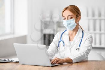 Female doctor wearing medical mask while using laptop in clinic�