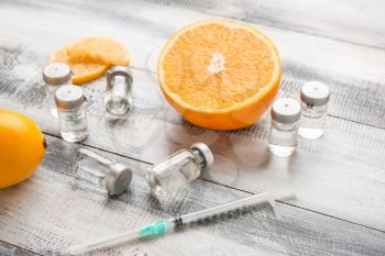 Ampules with vitamin C, syringe and citrus fruits on wooden background�