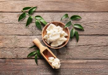 Plate and scoop with shea butter on wooden background�