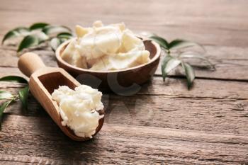 Plate and scoop with shea butter on wooden background�