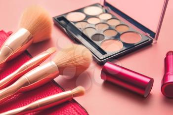 Bag with makeup brushes and cosmetics on color background�