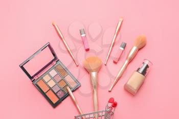 Shopping cart with makeup brushes and cosmetics on color background�
