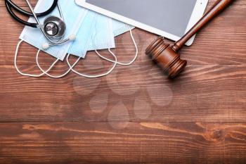 Judge gavel, tablet computer, masks and stethoscope on wooden background. Concept of health care reform�