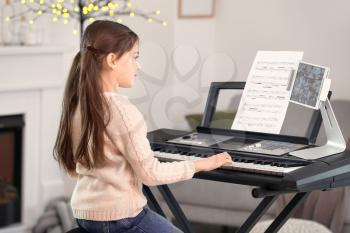Little girl taking music lessons online at home�