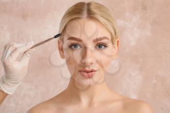 Young woman undergoing eyebrow correction procedure on color background�