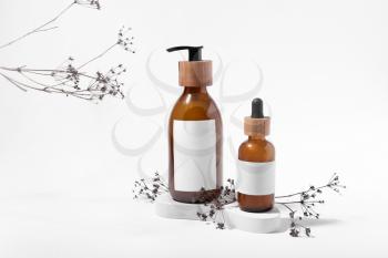 Bottles of natural hair cosmetics and flowers on white background�