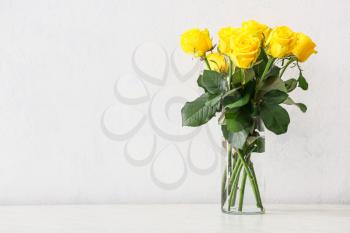 Vase with beautiful yellow roses on table against light background�