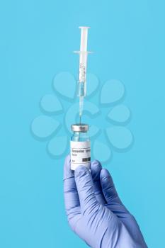 Doctor's hand with syringe and vaccine for immunization against COVID-19 on color background�