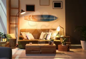 Interior of modern stylish room with surfboard and sofa in evening�