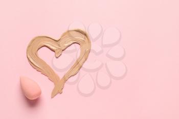 Sponge and heart made of makeup foundation on color background�