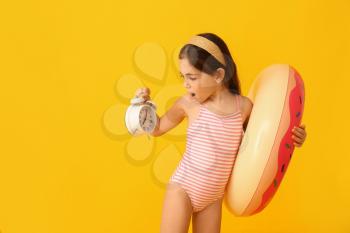 Surprised little girl in swimsuit, with alarm clock and inflatable ring on color background�