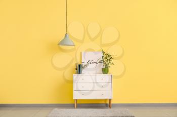 Stylish lamp and chest of drawers near color wall in room�