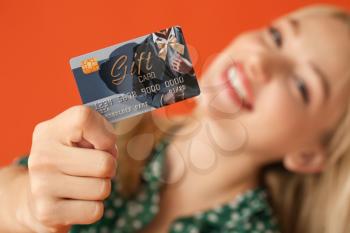 Beautiful young woman with gift card on color background�