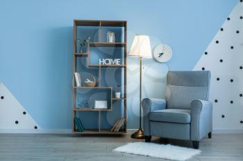 Glowing lamp with armchair and book shelf near color wall�