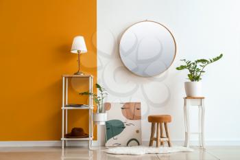 Modern lamp on table and mirror hanging on color wall in room�