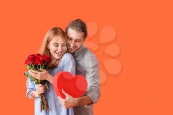 Young couple with flowers and gift on color background. Valentine's Day celebration�