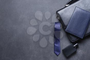 Stylish necktie with briefcase, perfume bottle and notebook on dark background�