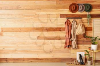 Hangers with clothes and hats on wooden wall�