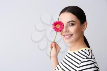 Beautiful young woman with flower on grey background�