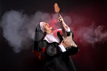 Young nun playing guitar on dark background�