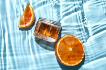 Jar of cosmetic product and cut orange in water on color background, closeup�