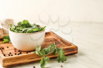 Board with fresh cilantro and peppercorns on light background�