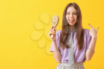 Funny young woman with hair brush on color background�