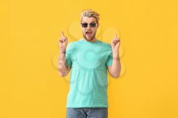 Young man with stylish sunglasses pointing at something on color background�