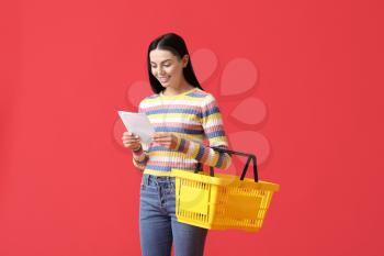 Young woman with shopping basket and list of products on color background�