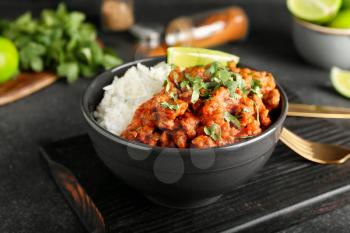 Bowl with tasty chili con carne, rice and lime on dark background, closeup�