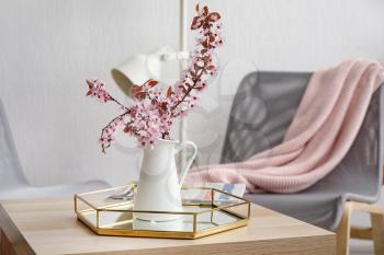 Jug with beautiful blossoming branches on table in room�
