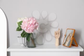 Vase with hydrangea flowers and decor on mantelpiece near light wall�