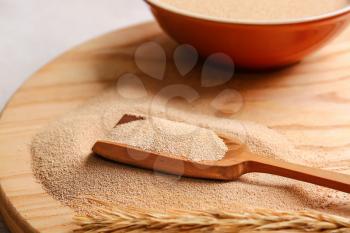 Scoop with active dry yeast on wooden board, closeup�
