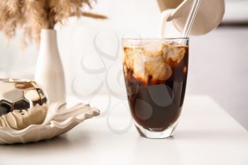 Pouring milk from jug into glass with tasty ice coffee on table, closeup�