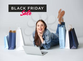 Young woman with laptop and shopping bags on grey background. Black Friday sale�