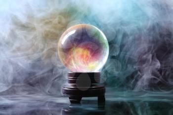 Crystal ball of fortune teller in smoke on table�