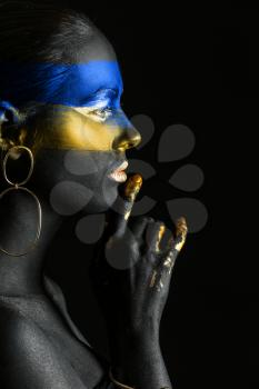 Young Ukrainian woman with blue and yellow paint on her body against dark background�