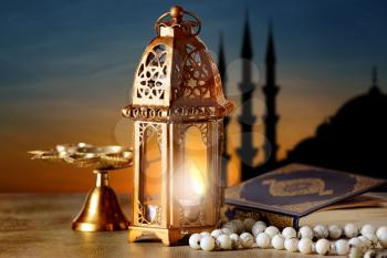 Muslim lamp, tasbih and Koran on table at sunset�