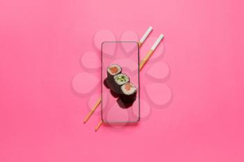 Tasty sushi rolls on screen of mobile phone and chopsticks on color background�