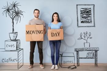 Young couple holding boxes with text MOVING DAY indoors and imagining interior of new house�