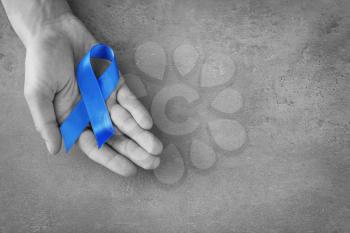 Male hand with blue ribbon on grey background. Prostate cancer concept�