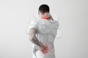 Young man suffering from back pain on light background�