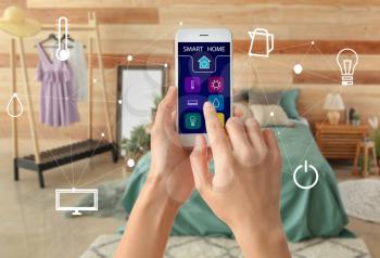 Woman using mobile phone application of smart home automation in room�