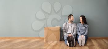 Young couple sitting on floor near box indoors. Moving into new house�