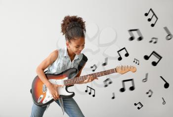 African-American girl playing guitar against light background 