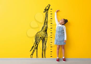 Surprised African-American girl measuring height near color wall with drawn giraffe�