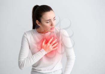 Young woman suffering from heart attack on light background�