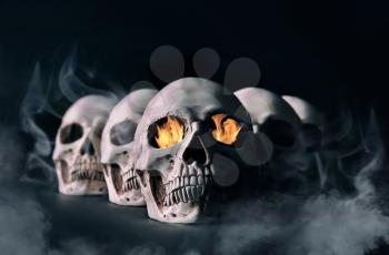 Human skulls with flame and smoke on dark background�